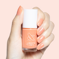 Hand holding Peeptoe quick dry polish bottle with matching sheer warm peach glossy manicure on short nails