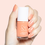 Hand holding Peeptoe quick dry polish bottle with matching sheer warm peach glossy manicure on short nails