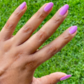 Hand with nails painted in bright floral purple pink shade using Petal - Gel against green grass background thumbnail