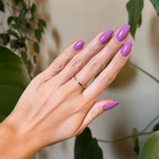 Hand with almond-shaped nails polished in bright floral purple pink using Petal - Gel against leafy natural backdrop