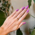 Hand with almond-shaped nails polished in bright floral purple pink using Petal - Gel against leafy natural backdrop thumbnail