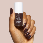 Hand holding Spressotini quick dry gel polish bottle with dark coffee brown manicure on medium nails against soft beige background