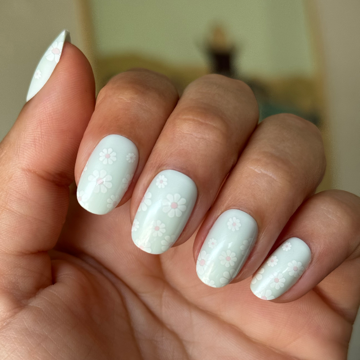 Teal Chrome Flower Shower - Press-On | Short | Round with pale teal nails and white daisy floral mani on hand indoors