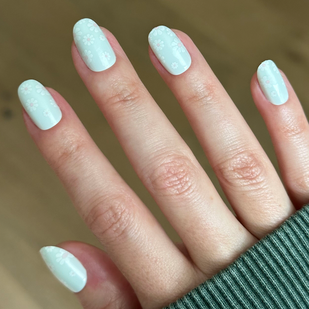 Teal Chrome Flower Shower - Press-On | Short | Round pastel teal press-on nails with subtle white daisy details on hand indoors
