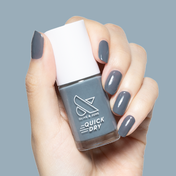 Hand holding Olive and June Torrential quick-dry gel polish bottle with matching moody slate grey manicure on short nails