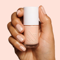 Hand holding Olive and June JO nail polish in a dusty apricot shade with matching polished nails for a chic mani look