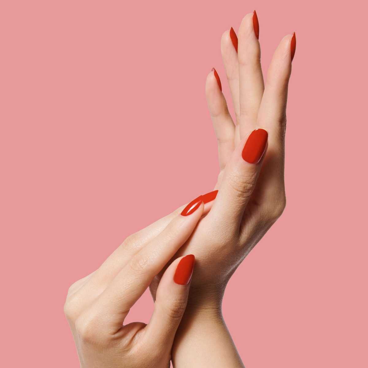 Hands with nails painted bright cherry red using CV polish by Olive and June on a soft pink background