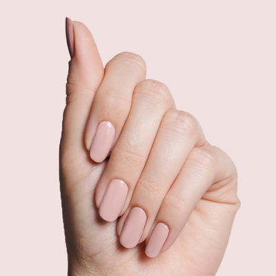 Hand holding Olive and June bottle with nails polished in HZ rosy neutral shade on light pink background HZ dusty rose Nail Polish