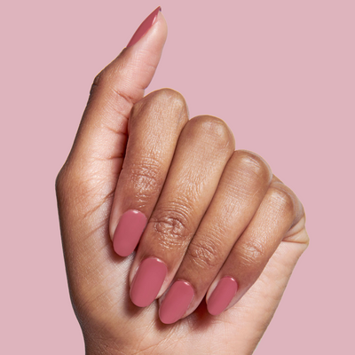 Hand holding Olive and June LD nail polish bottle with nails painted in a rosy pink shade for a polished mani look LD rosy neutral Nail Polish