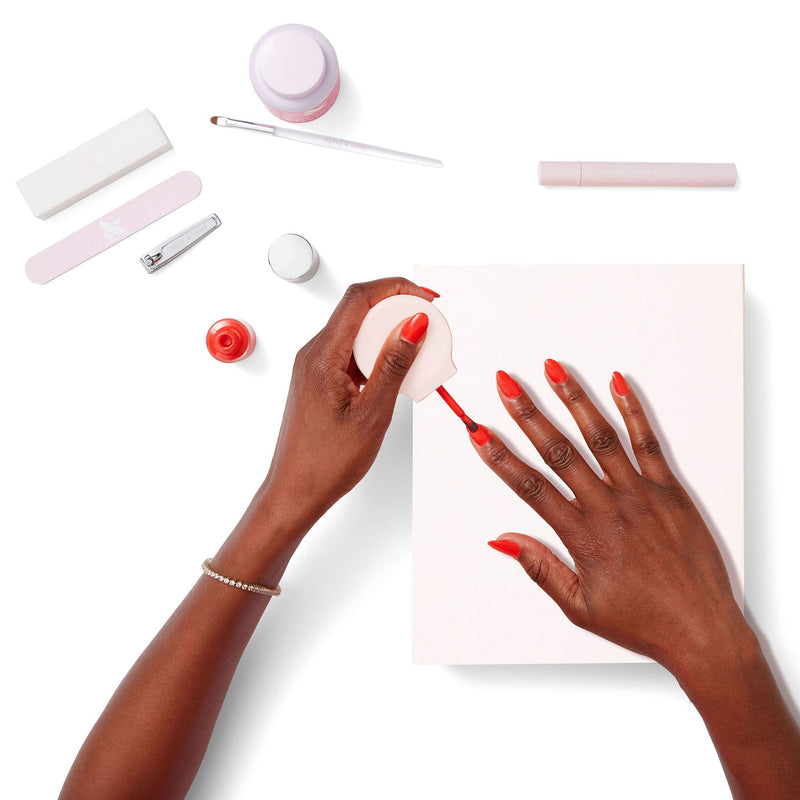 Hands applying bright red polish with manicure tools displayed on white background for Gift The Mani System