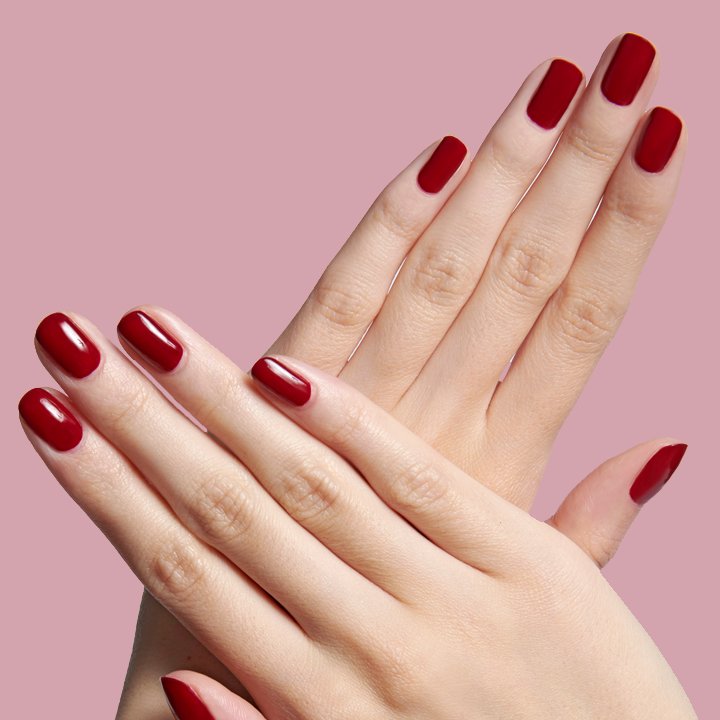 Close-up of hands with nails painted in deep burgundy SC polish showing a refined at-home manicure on soft pink background