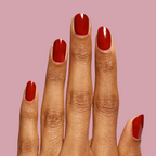 Hand with nails painted in glossy SC polish in deep bordeaux shade against soft mauve background showing elegant mani