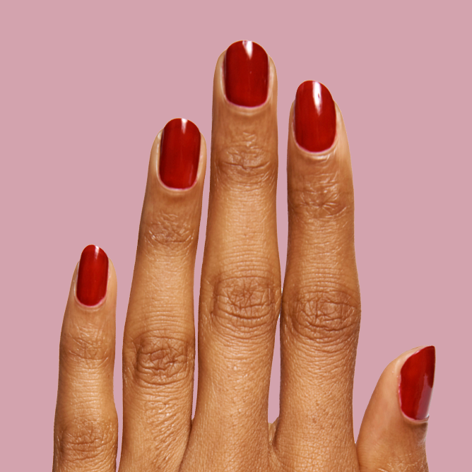 Hand with nails painted in glossy SC polish in deep bordeaux shade against soft mauve background showing elegant mani