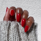 Hand with long nails painted in glossy rich scarlet red Smooch polish against textured white background and cozy knit sleeve