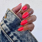 Hand with nails painted in bright orangey red Picante polish holding denim jacket for manicure display