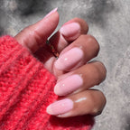 Hand with rounded nails painted in Potpourri sheer mauve gel polish wearing a red sweater in natural light