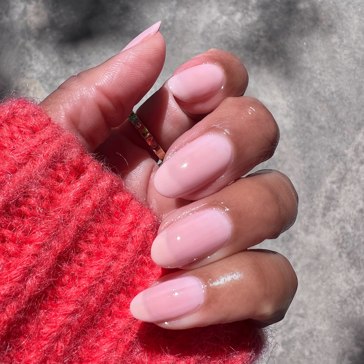 Hand with rounded nails painted in Potpourri sheer mauve gel polish wearing a red sweater in natural light