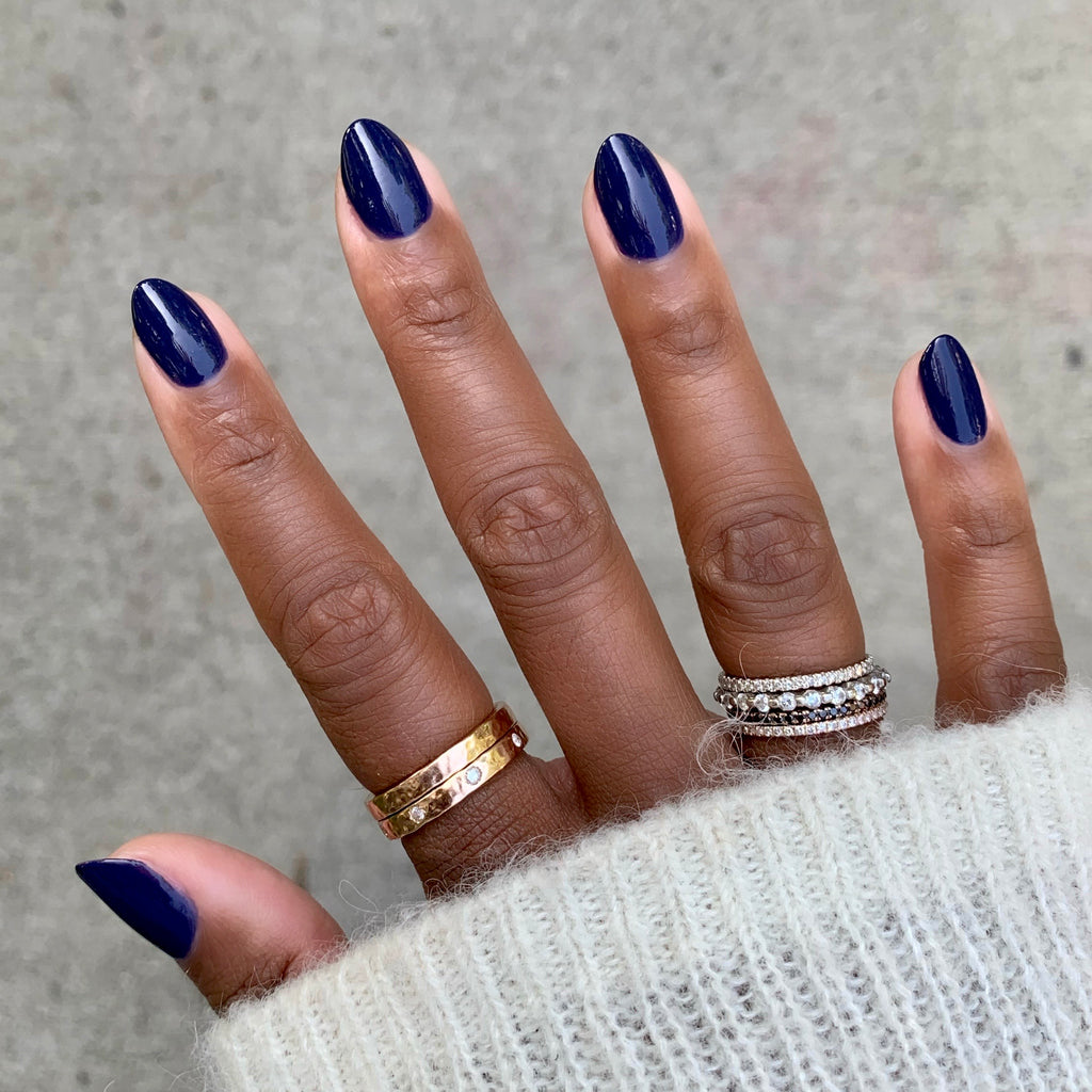 Hand with nails painted in glossy deep indigo OMG polish showing a smooth, long-lasting manicure with a cozy sweater sleeve