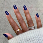 Hand with nails painted in glossy deep indigo OMG polish showing a smooth, long-lasting manicure with a cozy sweater sleeve
