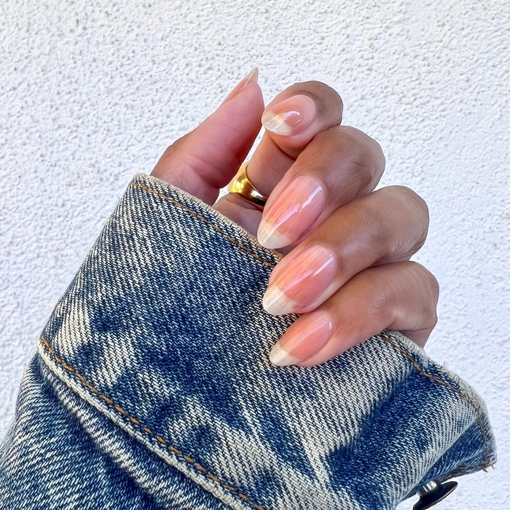 Hand with natural nails polished in Crystal clear coat holding a denim jacket sleeve showing a glossy manicure