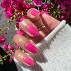 Hand with glossy magenta nails painted in This Lettuce is Radicchio polish by Olive and June holding sweater sleeve near pink flowers
