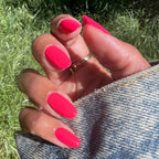 Hand with Pomodoro nail polish in bright pinky-tomato red on natural nails held over denim fabric outdoors