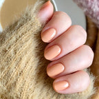 Hand with smooth nails painted in JO dusty apricot shade for a polished and cozy at-home manicure look