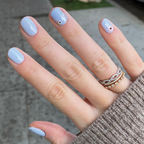 Hand with nails painted in BP, a pastel icy light blue gel polish with delicate floral accents for a fresh manicure