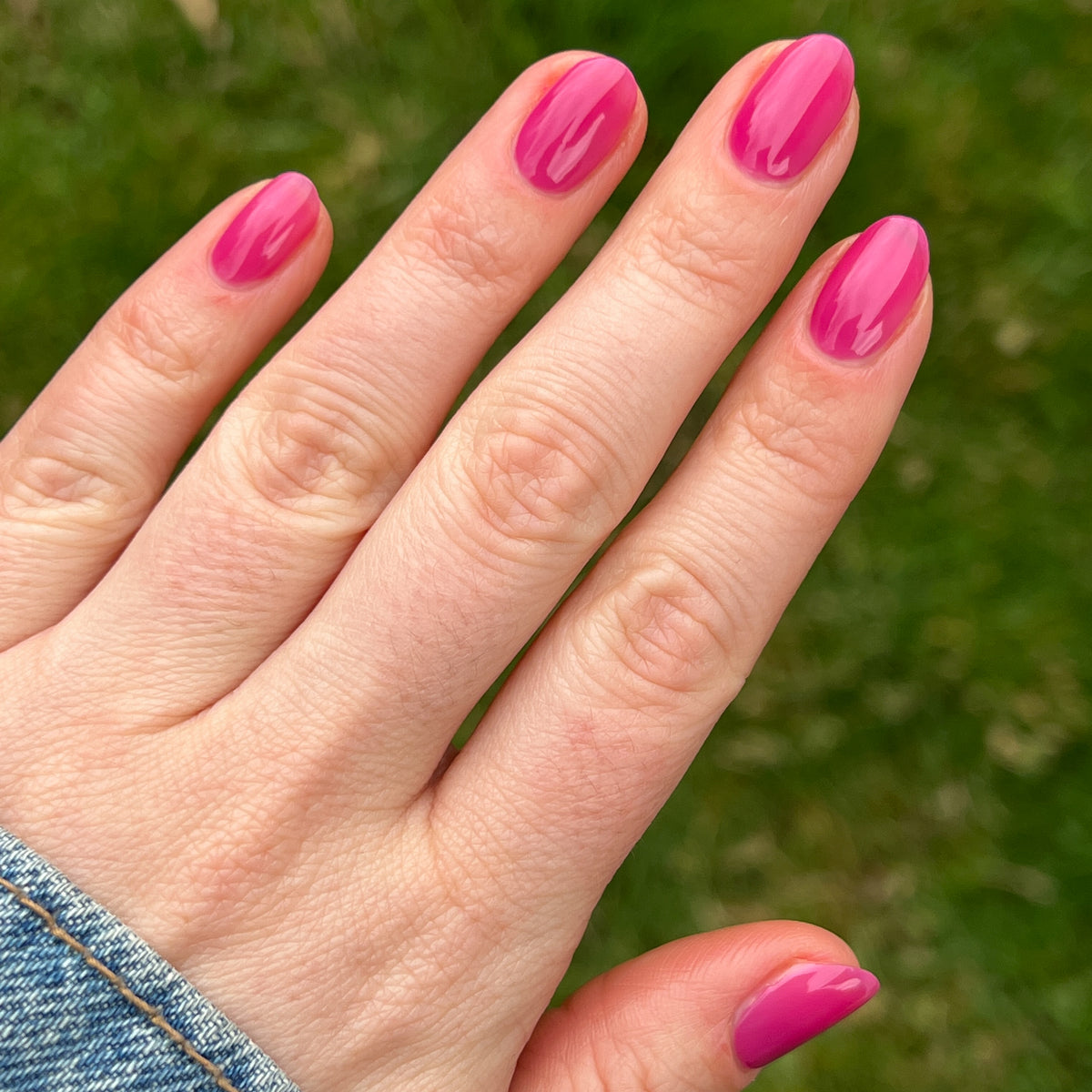 Hand displaying glossy nails painted with This Lettuce is Radicchio magenta-purple gel polish by Olive and June outdoors