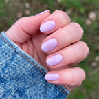 Hand with short nails painted glossy milky lavender in Lavender Stems gel polish by Olive and June outdoors
