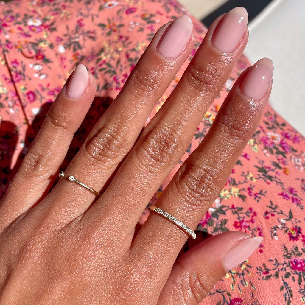 Hand with almond-shaped nails painted in sheer mauve Potpourri gel polish wearing delicate rings on floral fabric background