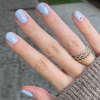 Hand with nails painted in BP, a pastel icy light blue gel polish with subtle nail art for a fresh at-home manicure