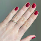 Hand with nails polished in SC deep bordeaux shade showcasing a glossy manicure against a soft neutral background