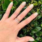 Hand with nails polished in Koala soft grey shade wearing gold rings against green leafy background for a fresh mani