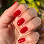 Hand with nails painted in bold glossy red shimmer Lippy polish displaying a bright at-home manicure in natural sunlight