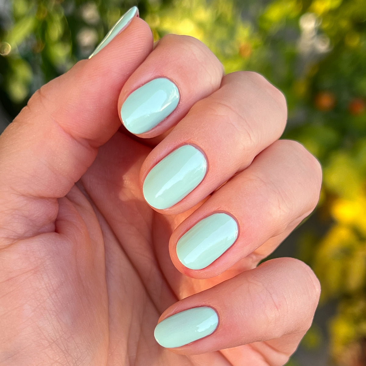 Hand with nails coated in glossy pastel green Minty polish for a fresh, at-home manicure by Olive and June