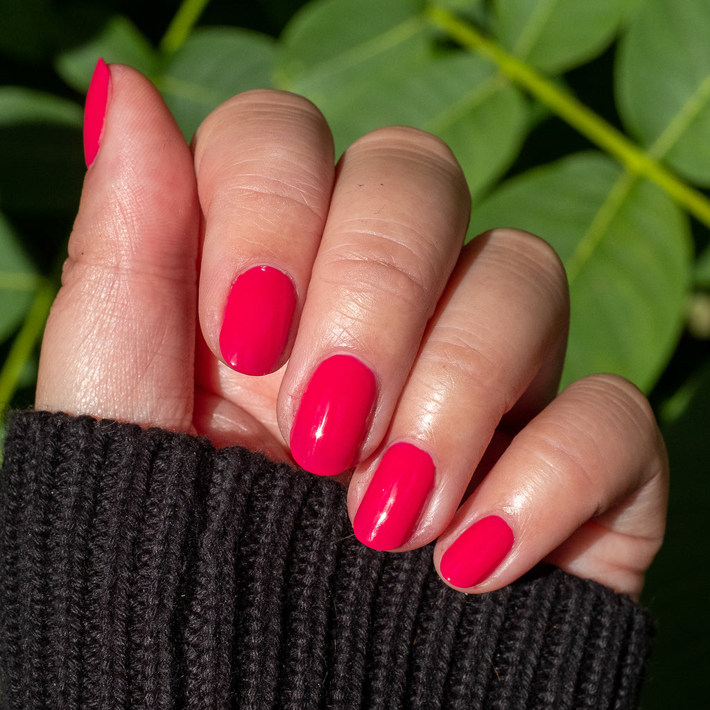 Hand displaying smooth nails painted with XOXO hot pink polish for a bright, long-lasting manicure outdoors