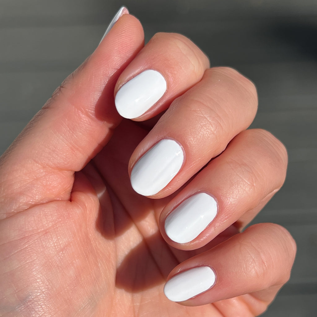 Fingernails painted in bright white Swan polish showcasing a smooth quick dry mani in natural daylight
