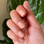 Hand with nails coated in JO polish showcasing a creamy dusty apricot shade for a fresh at-home manicure look