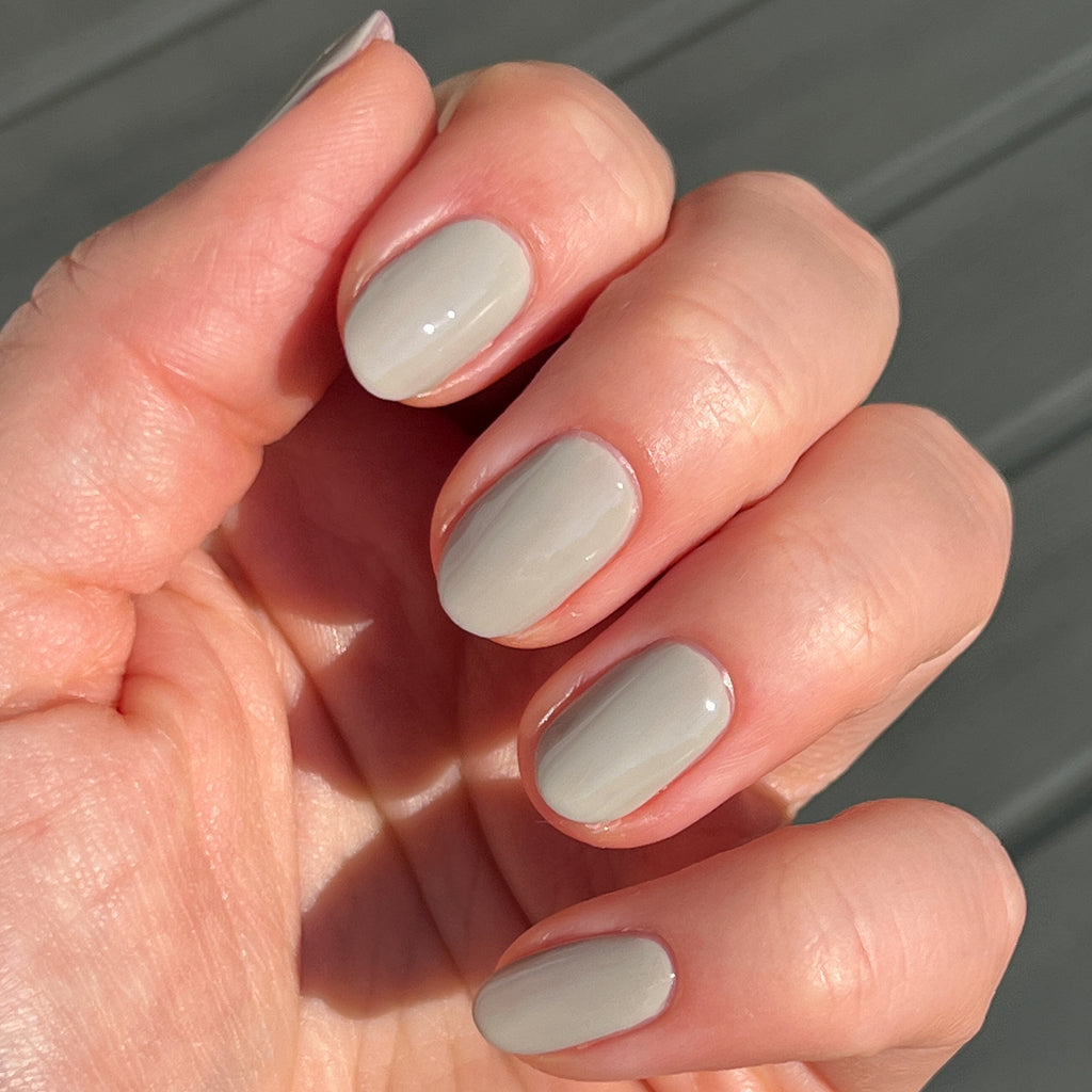 Hand with nails coated in Koala neutral soft grey polish shown in natural light for a smooth manicure look