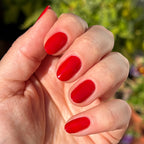 Hand with nails painted in glossy vibrant red Smooch polish shown in natural outdoor light for manicure display