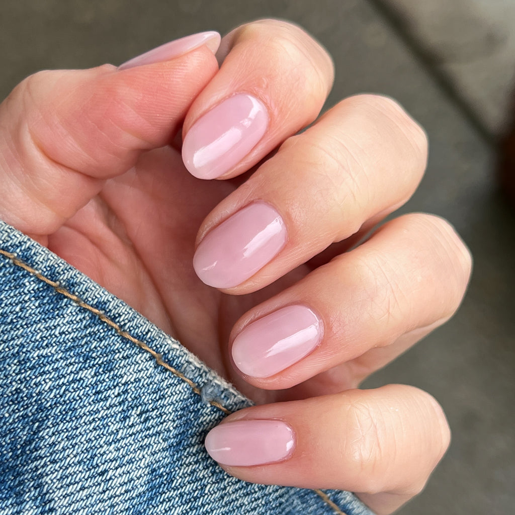 Hand with short nails coated in Potpourri sheer mauve quick dry gel polish holding denim fabric