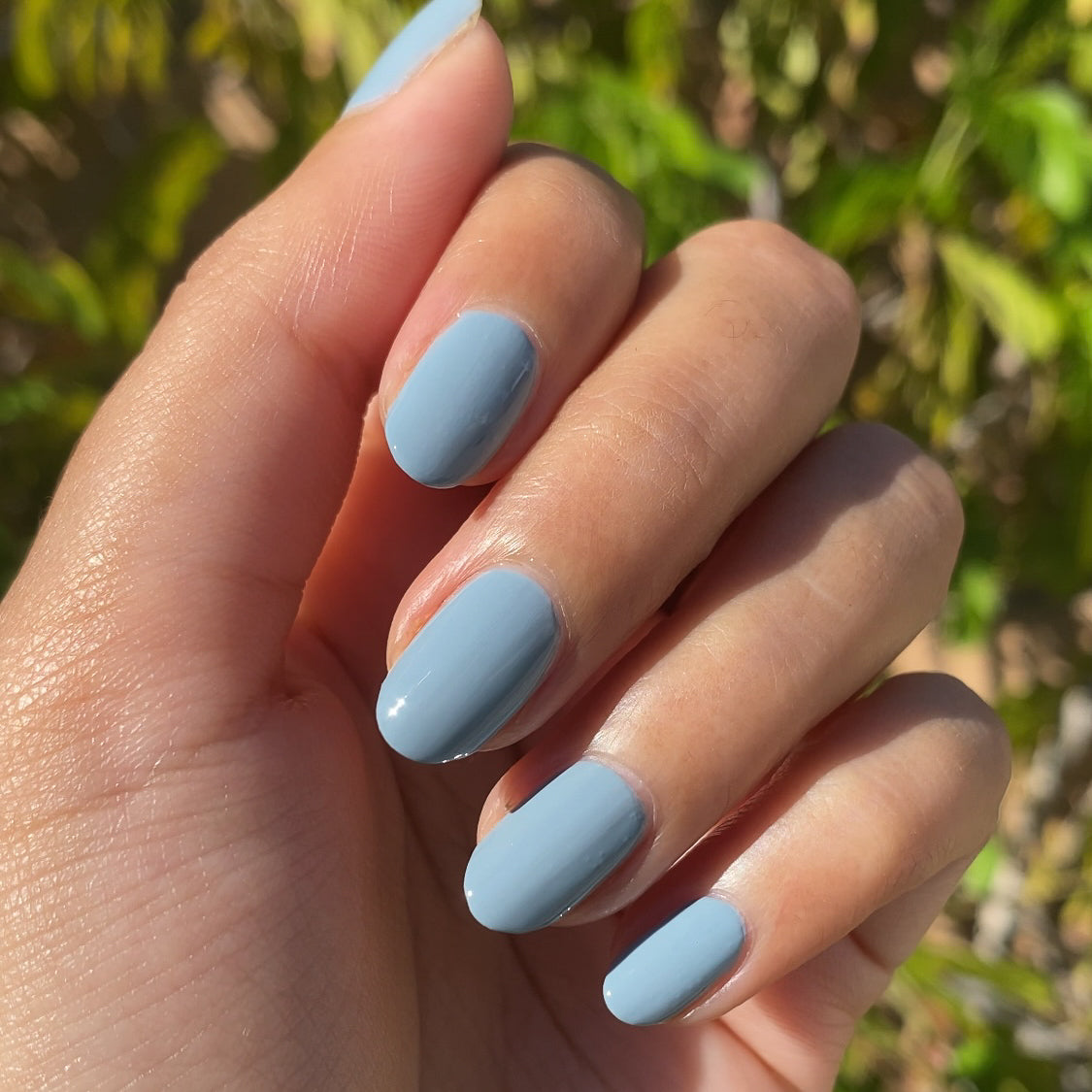 Hand showing nails painted in Vintage denim blue polish for a smooth, glossy at-home manicure look
