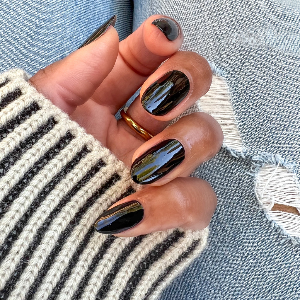 Hand with glossy Cateye polish on medium-length nails wearing a striped sweater and gold ring over ripped jeans