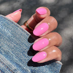 Hand with glossy bright pink Taffy gel polish on nails holding denim jacket sleeve in natural sunlight manicure view