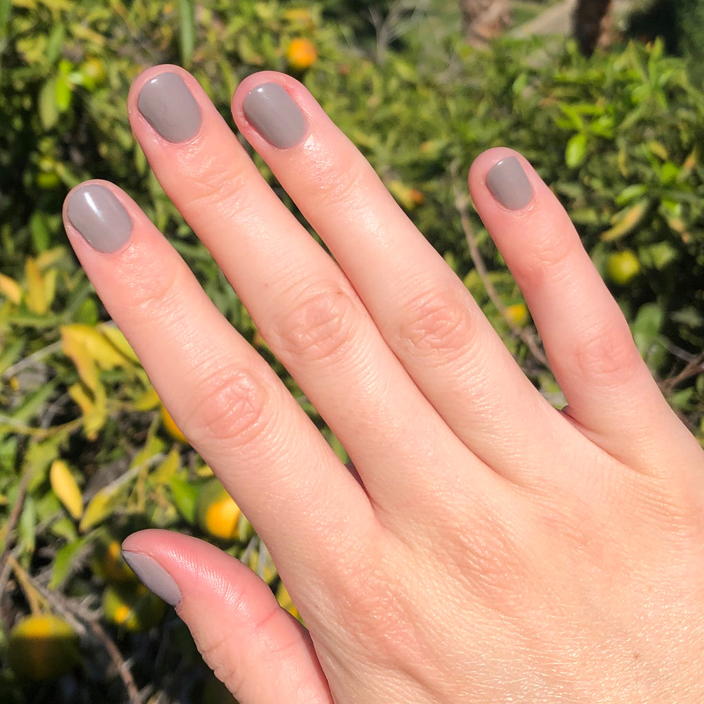 Hand with nails painted in AW warm toned grey showing a smooth, glossy manicure in natural sunlight outdoors