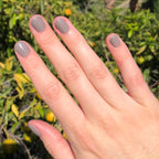 Hand with nails painted in AW warm toned grey showing a smooth, glossy manicure in natural sunlight outdoors