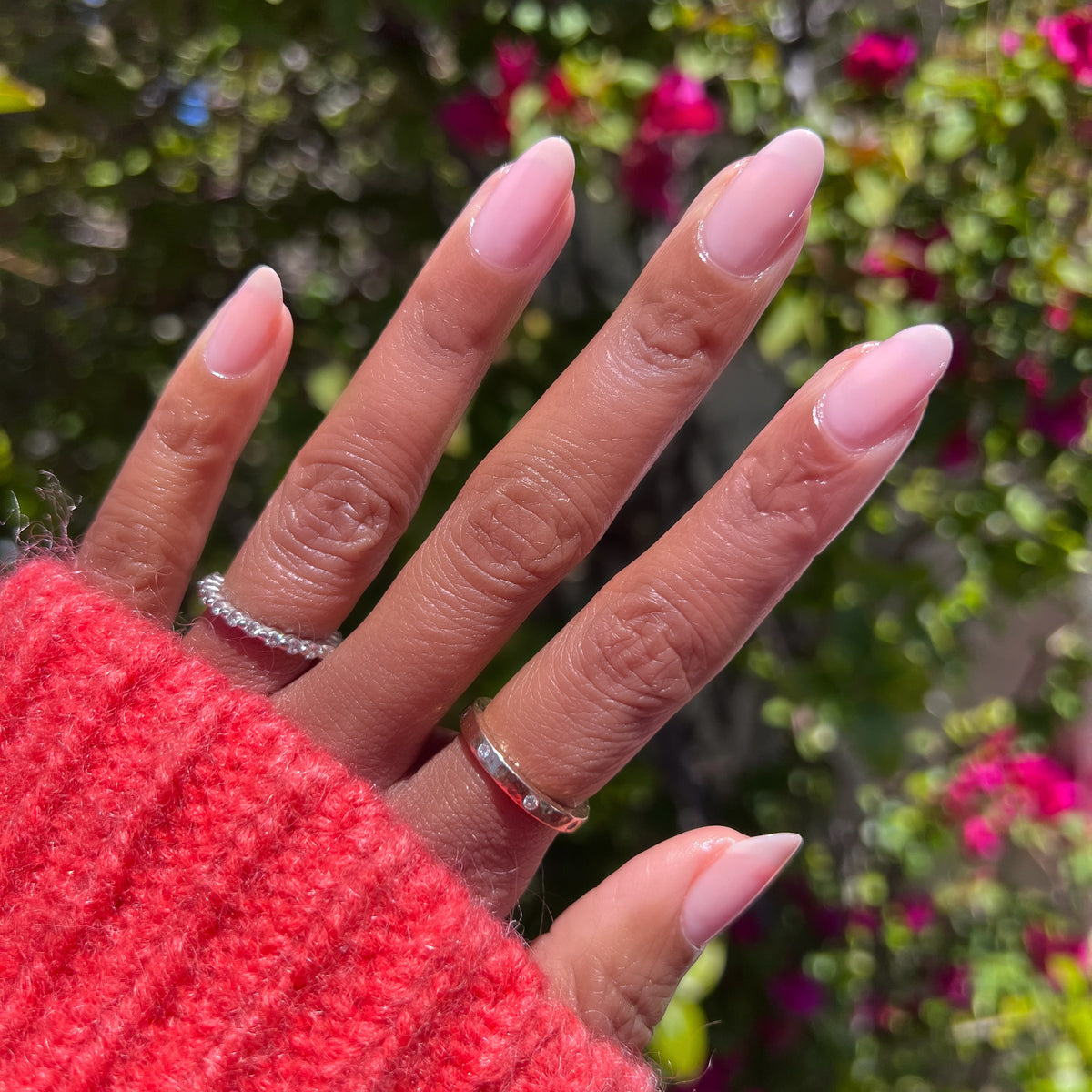 Hand with long almond nails painted in Potpourri sheer mauve gel polish wearing rings outdoors in natural light