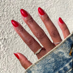 Hand with nails painted in shimmery glossy red Lippy polish displaying a bright at-home mani in sunlight