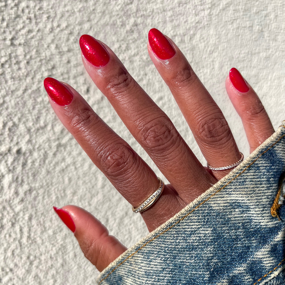 Hand with nails painted in shimmery glossy red Lippy polish displaying a bright at-home mani in sunlight